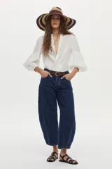 Camisa de lino color beige, con escote en V, cuello mao y mangas abullonadas tres cuartos. Cuenta con cierre frontal de botones y tiras ajustables para atar en la cintura.