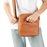 Bandolera de cuero color habano con textura granulada, cierre superior y bolsillo frontal abierto. Cuenta con una correa de tela ajustable con detalle de marca grabado.