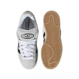 Championes urbanos adidas modelo Campus 00s, confeccionados en gamuza color gris claro con las icónicas tres tiras laterales en color negro. Presentan cordones blancos, suela de goma color crema y una base de goma natural.