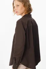 Camisa blanca de corte clásico con cuello camisero y cierre frontal de botones. Presenta un bordado lineal en color marrón oscuro en ambos lados del frente, representando motivos florales.