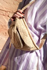 Riñonera color beige con textura de piel de cocodrilo, correa ajustable y cierre con cremallera.