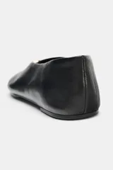 Bailarina plana de piel negra con acabado suave, escote en pico y detalle metálico dorado en la parte frontal. Presenta pespuntes decorativos y punta redonda.