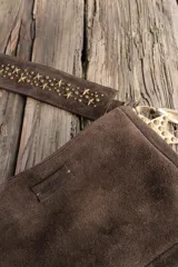 Bandolera confeccionada en cuero de gamuza marrón, con cierre superior. Presenta un llavero colgante con forma de estrella revestido en tachas metálicas y tiras flecadas en tono dorado.