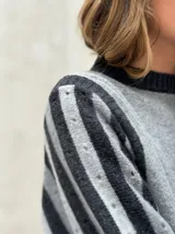 Sweater de lana color crudo con mangas largas abullonadas en gris y blanco, con diseño de rayas y perforaciones. Cuello redondo y puños acanalados.