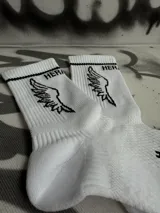 Par de medias blancas de algodón con puño acanalado con una línea negra, logo de la marca en el tobillo y estampado de alas negras.