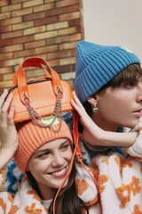 Cartera de mano naranja de cuero sintético con doble asa corta, cierre superior con doble cremallera y cadena metálica plateada decorativa. Incluye correa extraíble y ajustable.