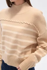 Sweater de punto color beige con rayas horizontales color crema, cuello alto y corte holgado. Presenta costuras decorativas en hombros y pecho.