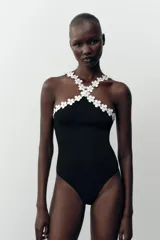 Body negro de tejido elástico con escote halter y detalle de flores blancas aplicadas en el contorno.
