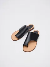 Sandalias planas de cuero color marrón, con diseño minimalista que sujeta el dedo pulgar y deja el empeine al descubierto.