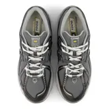 Championes New Balance modelo 1906R, color gris oscuro con detalles en gris claro, blanco y amarillo. Presentan una parte superior de malla transpirable con superposiciones sintéticas y el logo "N" en los laterales.