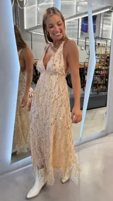 Vestido largo beige con escote en V pronunciado, tirantes finos cruzados en la espalda y diseño holgado cubierto de lentejuelas doradas dispuestas en patrones ondulados.