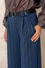 Pantalón de corte ancho y tiro alto, confeccionado en tejido azul marino con finas rayas verticales de hilo de lurex plateado. Presenta cintura con pasacintos y se incluye un cinturón negro con hebilla metálica.