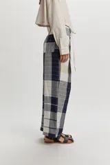 Pantalón Tokyo de lino con diseño a cuadros en tonos azul marino, beige y blanco. Presenta un corte amplio y relajado, cintura con cierre frontal de botón y tiras decorativas colgantes.