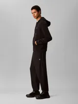 Jogger de felpa Calvin Klein color negro, con cintura elástica, bolsillos laterales y puños acanalados en los tobillos. Presenta el monograma de la marca bordado discretamente en la pierna.