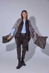 Ruana tejida en lana lambswool con diseño de bloques de color y tramas geométricas. Presenta cierre frontal con doble cursor y tiradores de cuero, permitiendo diferentes formas de uso.