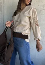 Blusa color beige con escote en V, manga larga y detalles de encaje calado en los hombros.
