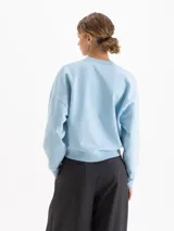 Buzo de cuello redondo y mangas largas, con silueta amplia y largo a la cadera. Presenta un estampado gráfico frontal de estilo urbano con temática de mercado y un conejo, parte de una colaboración artística.