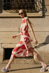 Vestido midi de color beige con estampado floral en tonos rojos y fucsias, con cuello fluido, manga sisa y cinturón del mismo tejido.