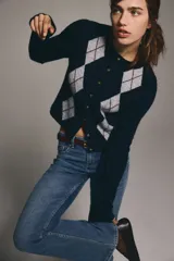 Jeans de denim azul medio con ligero efecto desgastado, tiro bajo y corte acampanado (bootcut) desde la rodilla. Presenta cierre y botón frontal, bolsillos delanteros decorativos y bolsillos abiertos traseros.