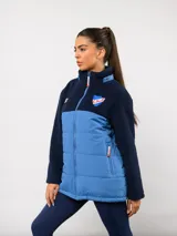 Parka de abrigo Umbro del Club Nacional de Football, con diseño bicolor que combina tejido polar blanco en la parte superior y tejido acolchado azul marino en la parte inferior. Cuenta con cierre frontal completo, cuello alto y bolsillos laterales.