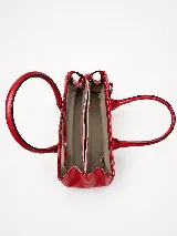 Cartera de mano estructurada de cuero vacuno rojo, con doble asa superior y detalles de charol en la parte superior. Cuenta con cierres metálicos y apliques decorativos laterales con hebillas.