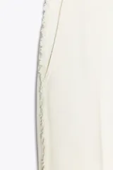 Pantalón de tiro alto color crudo, de pernera recta con detalle de bandas laterales desflecadas.