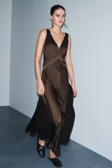 Vestido largo de satén color marrón oscuro, con escote en pico pronunciado, tirantes anchos y bajo en línea evasé con abertura lateral.