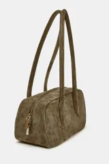 Bolso de hombro de formato alargado confeccionado en gamuza color marrón. Cuenta con doble asa de hombro y cierre superior mediante cremallera metálica.