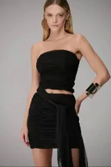 Blusa strapless de tul negro con diseño drapeado en todo el cuerpo, silueta ajustada y faixa incorporada en la cintura que aporta movimiento.