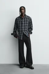 Camisa de corte relajado confeccionada en tejido fluido de cupro y viscosa, con estampado de cuadros, cuello solapa, manga larga con puño abotonado y cierre frontal de botones.