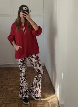Conjunto compuesto por un canguro rojo de corte holgado con capucha, cordones ajustables y bolsillo frontal tipo canguro, y un pantalón de tiro alto con corte acampanado y estampado abstracto en tonos bordó, blanco y beige.