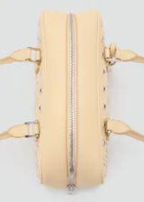 Bolso tipo bowling de color beige, adornado con múltiples ojales metálicos plateados en la parte frontal. Cuenta con doble asa de mano superior y cierre con cremallera.