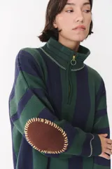 Buzo de punto con diseño a rayas verticales en tonos verde y azul marino. Presenta cuello alto con cierre frontal parcial, hombros caídos y coderas en contraste de color marrón con costuras decorativas visibles.