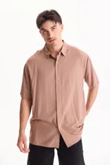 Camisa oversize de manga corta color tostado, con cuello camisero y cierre frontal con botones.