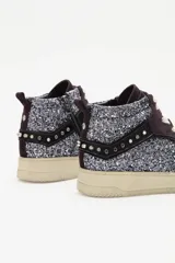 Zapatilla de caña media con paneles de gamuza bordó y laterales cubiertos de glitter plateado. Presenta detalles de tachas metálicas en la parte trasera, cordones blancos y suela de goma blanca.