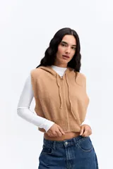 Chaleco de punto color beige, de corte corto y holgado. Presenta capucha, cierre frontal completo y terminaciones acanaladas en la cintura.