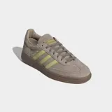 Championes Adidas modelo Handball Spezial, confeccionados en gamuza color marrón con las icónicas tres rayas laterales y detalles en color verde lima. Presentan suela de caucho color caramelo y el logo Spezial en el lateral.