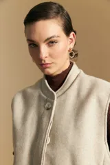 Chaleco de paño color marrón oscuro, de silueta recta y diseño minimalista. Presenta cuello a la base, cierre frontal con botones claros y bolsillos aplicados.