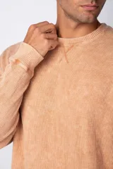 Buzo de corte oversize confeccionado en tela waffle de algodón con proceso de teñido acid wash. Presenta cuello redondo con detalle de costura en X y mangas largas con puños acanalados.