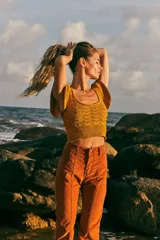 Top tejido de punto color naranja con destellos de lurex, escote redondo y mangas con volados. Presenta un diseño ajustado con cintura elástica acanalada.