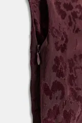 Vestido midi asimétrico de un solo hombro en color bordó, confeccionado en tejido devoré con diseño floral y detalles de terciopelo. Presenta frunces laterales, bajo con flecos largos y aplicación de tachas metálicas. Incluye forro interior y cierre lateral con cremallera oculta.