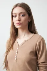 Remera de manga larga color beige, confeccionada en algodón, con escote en V y cartera corta de botones blancos.