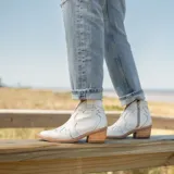 Botín de cuero vacuno color marrón oscuro, con taco de madera foliado en cuero de 5cm de altura, cierre lateral interno y horma de punta fina.