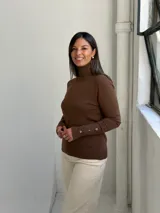 Polera de tejido de punto color chocolate, con cuello alto y mangas largas que presentan detalles de botones dorados en los puños.