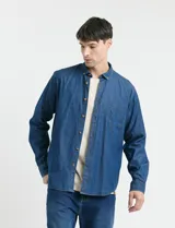 Camisa de jean de manga larga con cuello clásico, cierre frontal con botones y bolsillo tipo parche en el pecho.