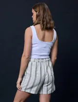 Short color crema con finas rayas verticales grises, pretina elastizada con cordón de ajuste, bolsillos delanteros y traseros.