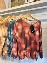 Remera de manga larga con diseño estampado de flores en tonos marrones y destellos de lurex. Presenta un corte holgado, cuello redondo y puños en color gris claro.