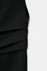 Vestido midi negro de cuello redondo y manga sisa, con detalle de drapeado en la cintura y cierre lateral con cremallera oculta.