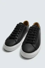 Zapatilla de cordones color negro con parte superior lisa, horma redonda y forro interior a contraste. Suela de goma color crema con ligera textura y detalle en el talón color crema.