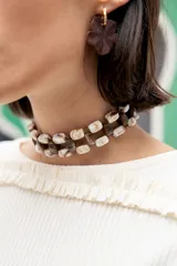Gargantilla tipo choker de doble hilera, confeccionada con cuentas rectangulares de acrílico en tonos marmolados beige y marrón oscuro. Presenta un diseño trenzado y cierre ajustable con cadena de acero quirúrgico.